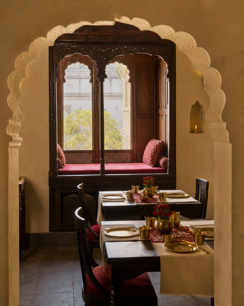 Warmly lit jharokha dining alcove with carved wood and brass table settings