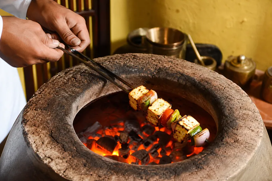 Paneer tikka roasting over glowing coals in a clay tandoor